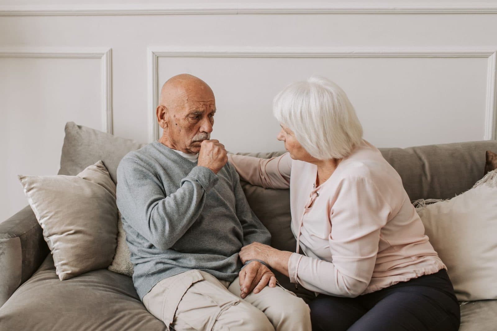 Older man coughing on a couch while his wife comforts him