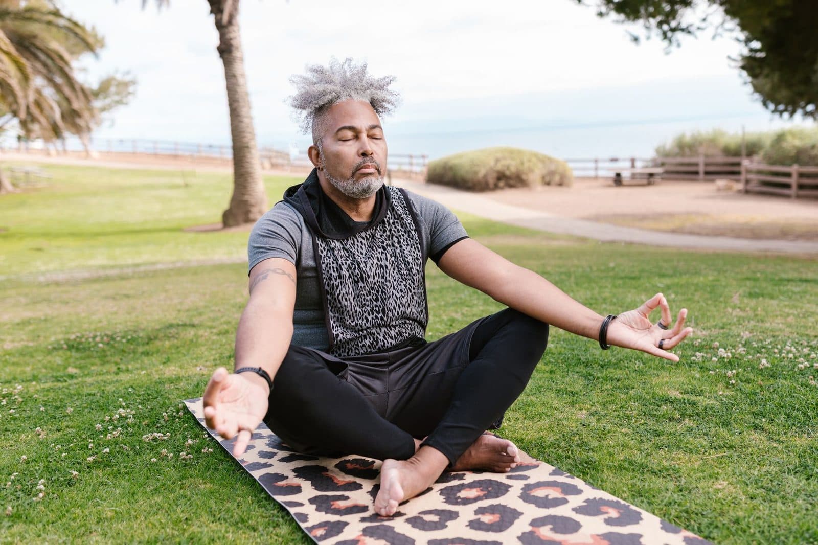 Older man breathing deeply while sitting cross-legged in a park