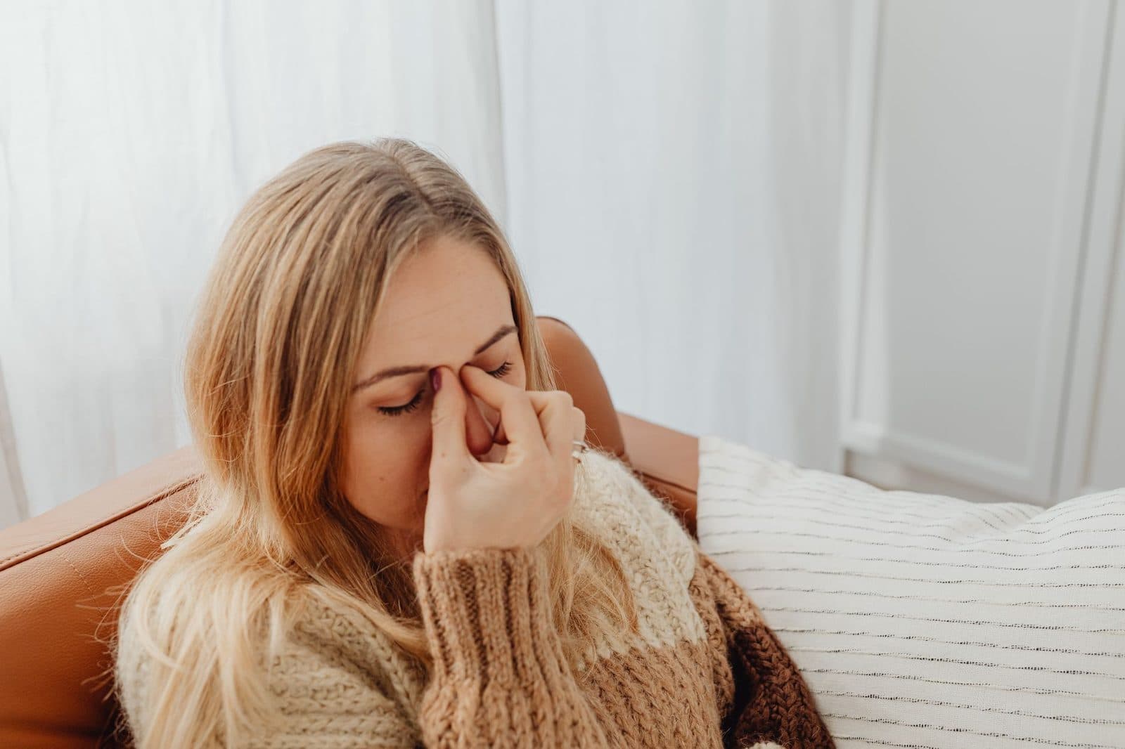 Woman on a couch pinching the bridge of her nose from sinus pressure